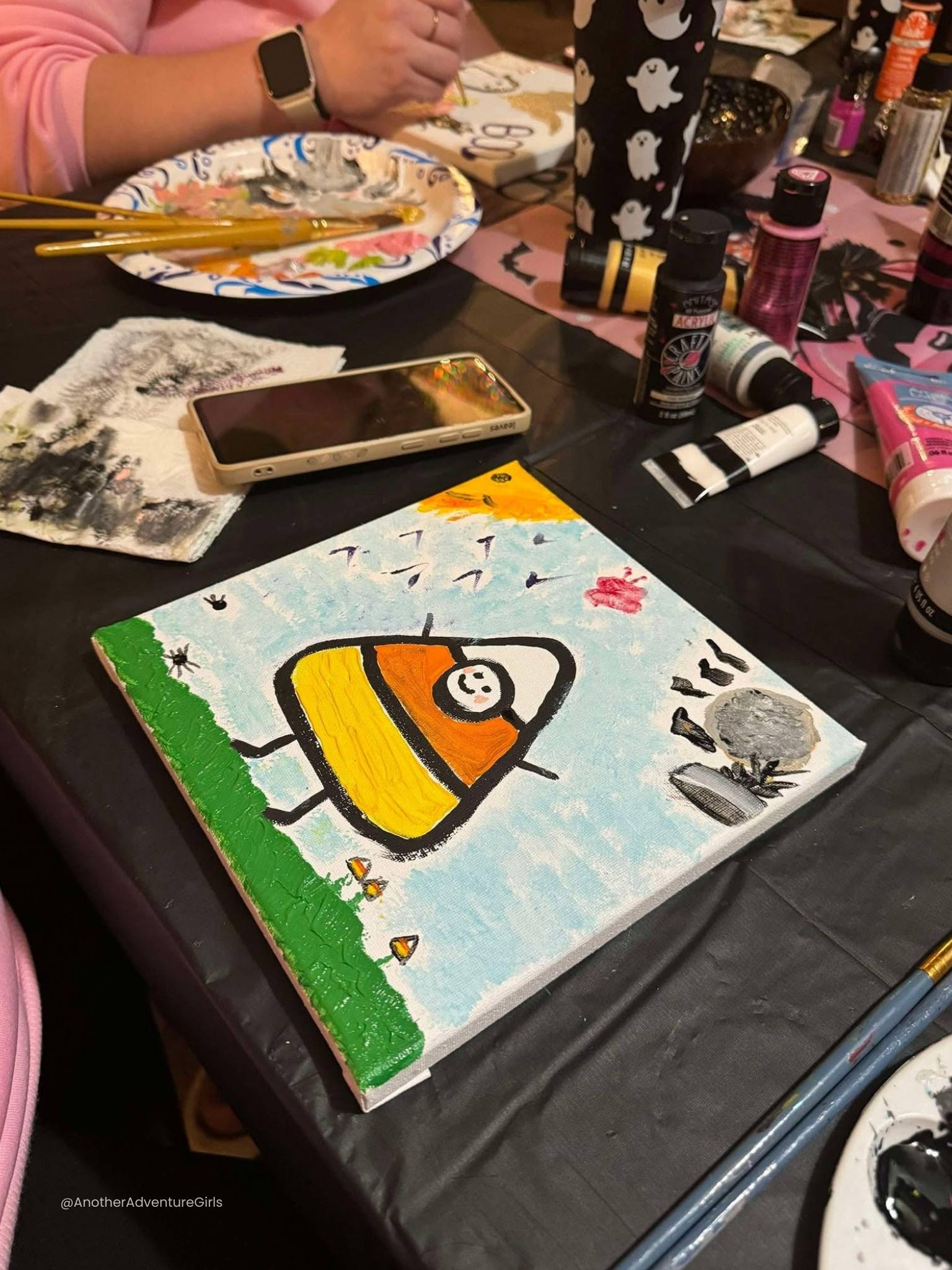 a painting of a large candy corn with a smiling face and tiny arms and legs standing on grass with a blue sky and sun in the upper left corner