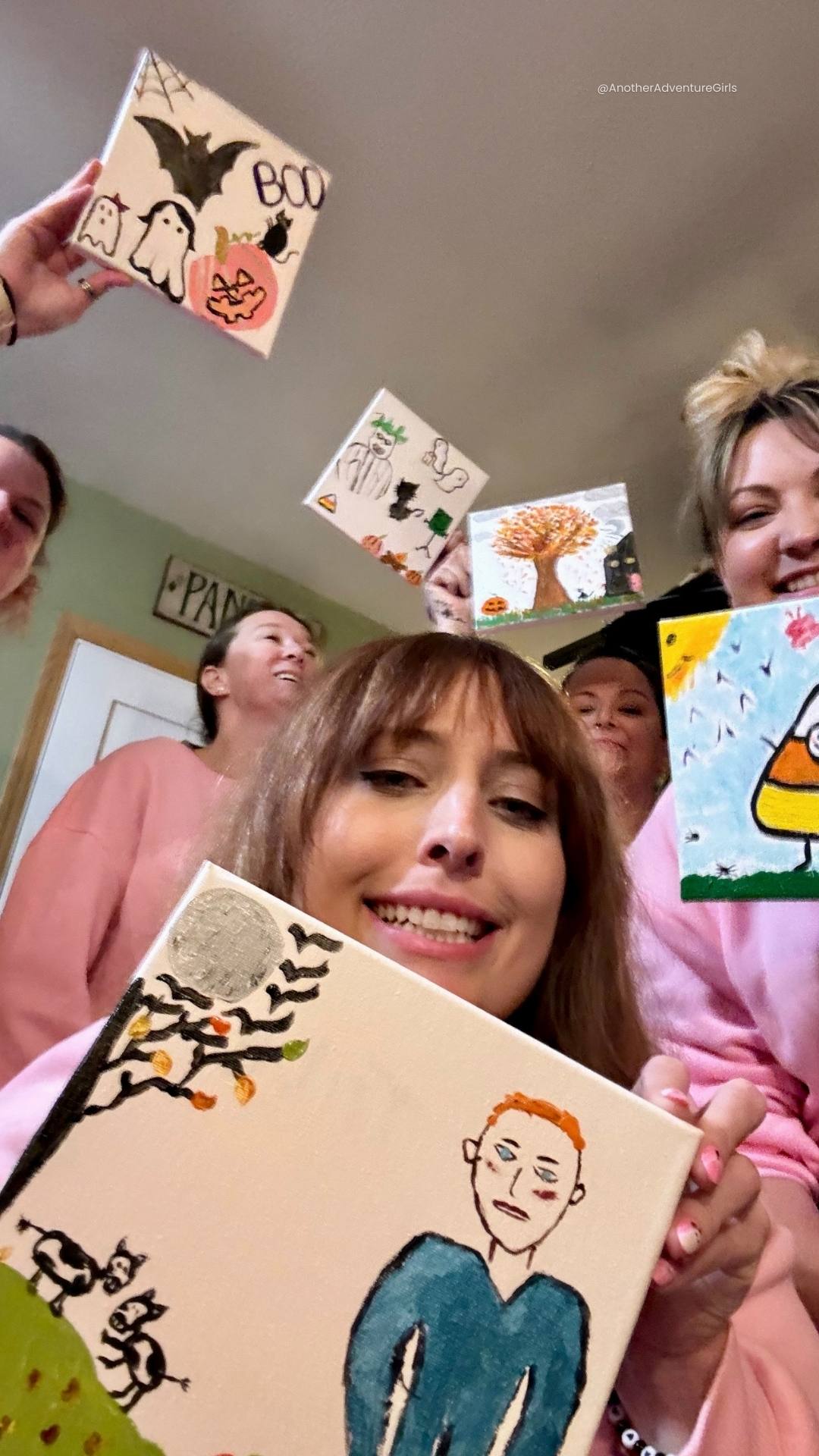 five women gathered for a selfie each holding up their finished 12x12 canvas Halloween painting