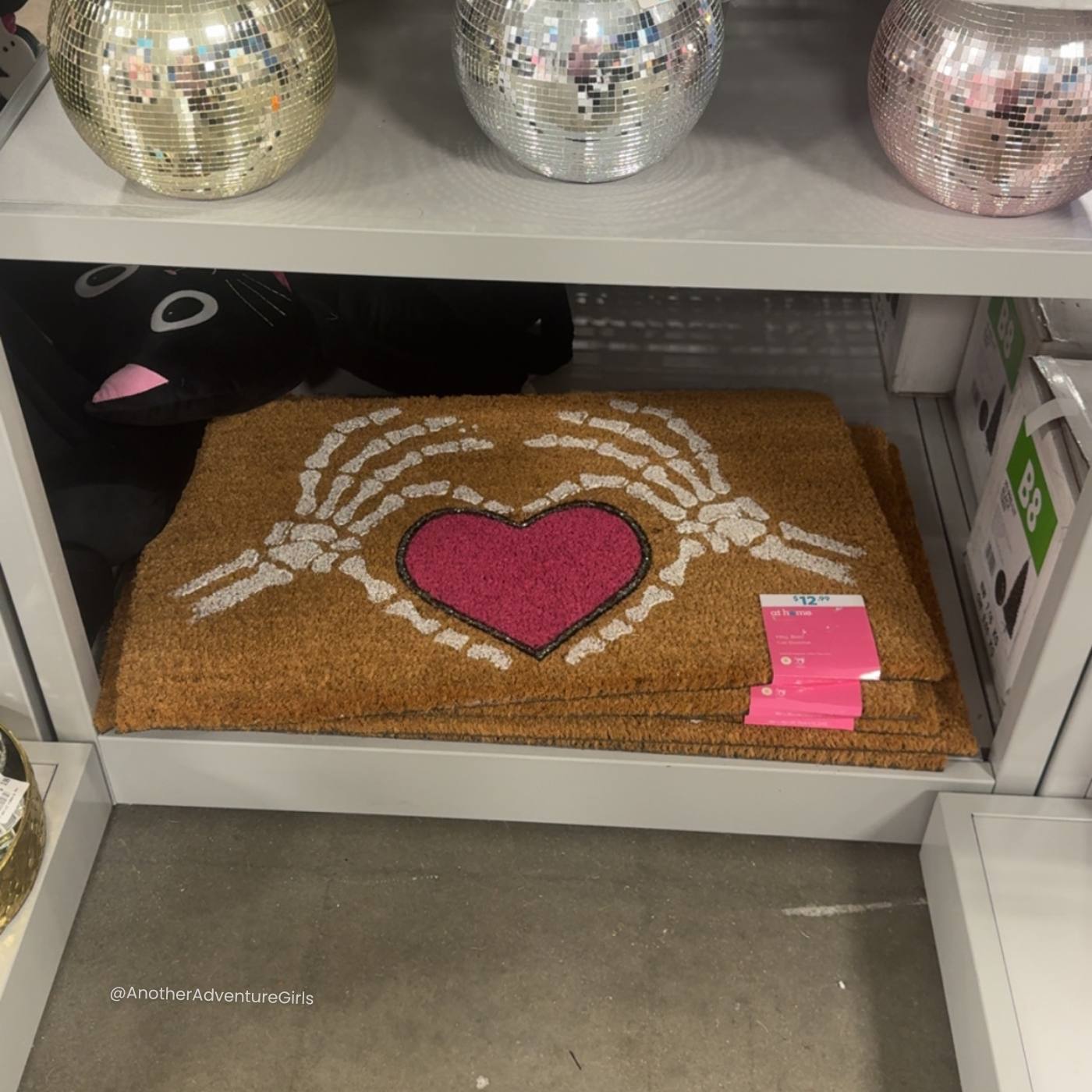 coir doormat with a pink heart in the center, surrounded by white skeleton hands making a heart shape around the pink heart