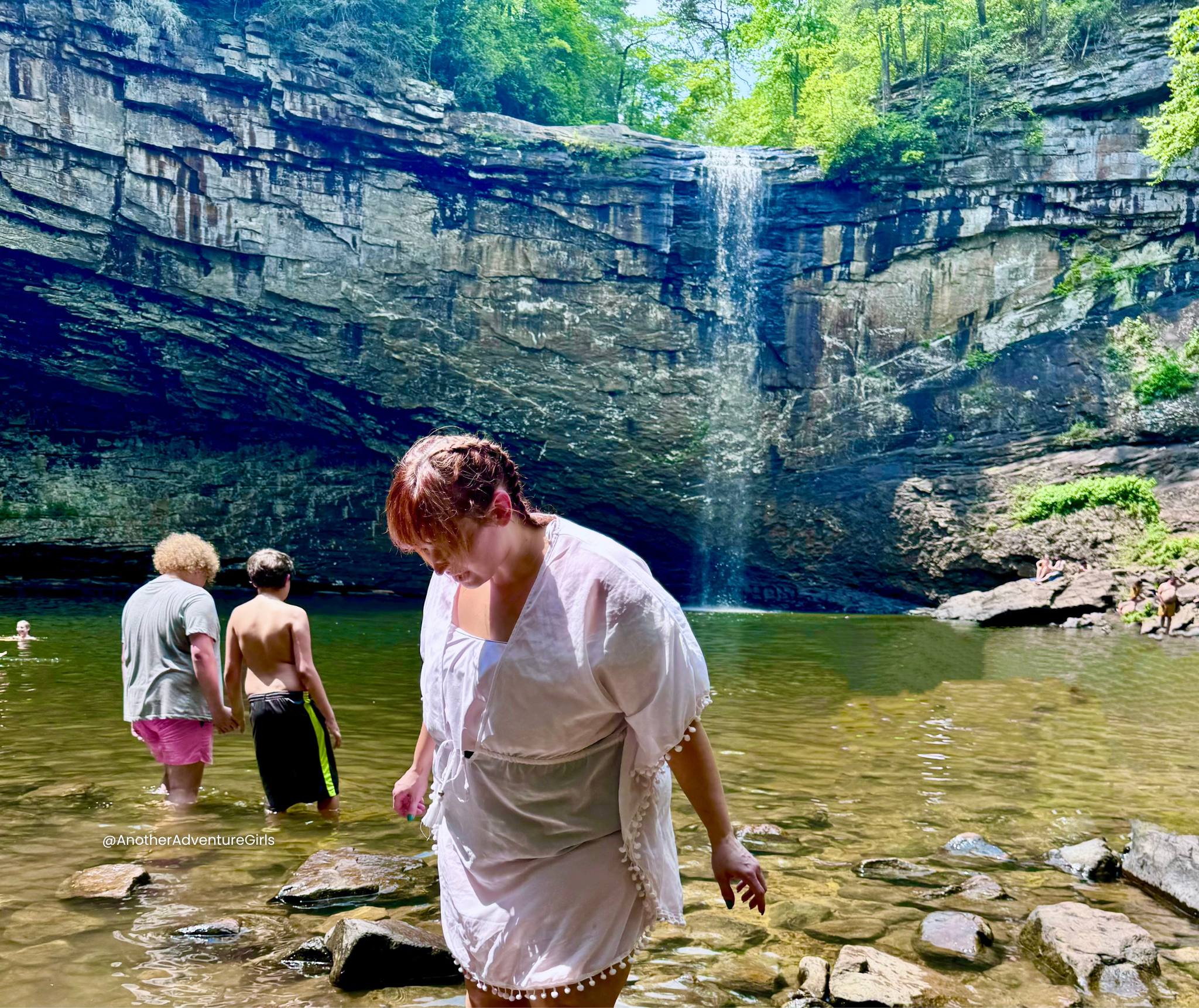 Erin looking down with kids to the left of her in the water in front of Foster Falls