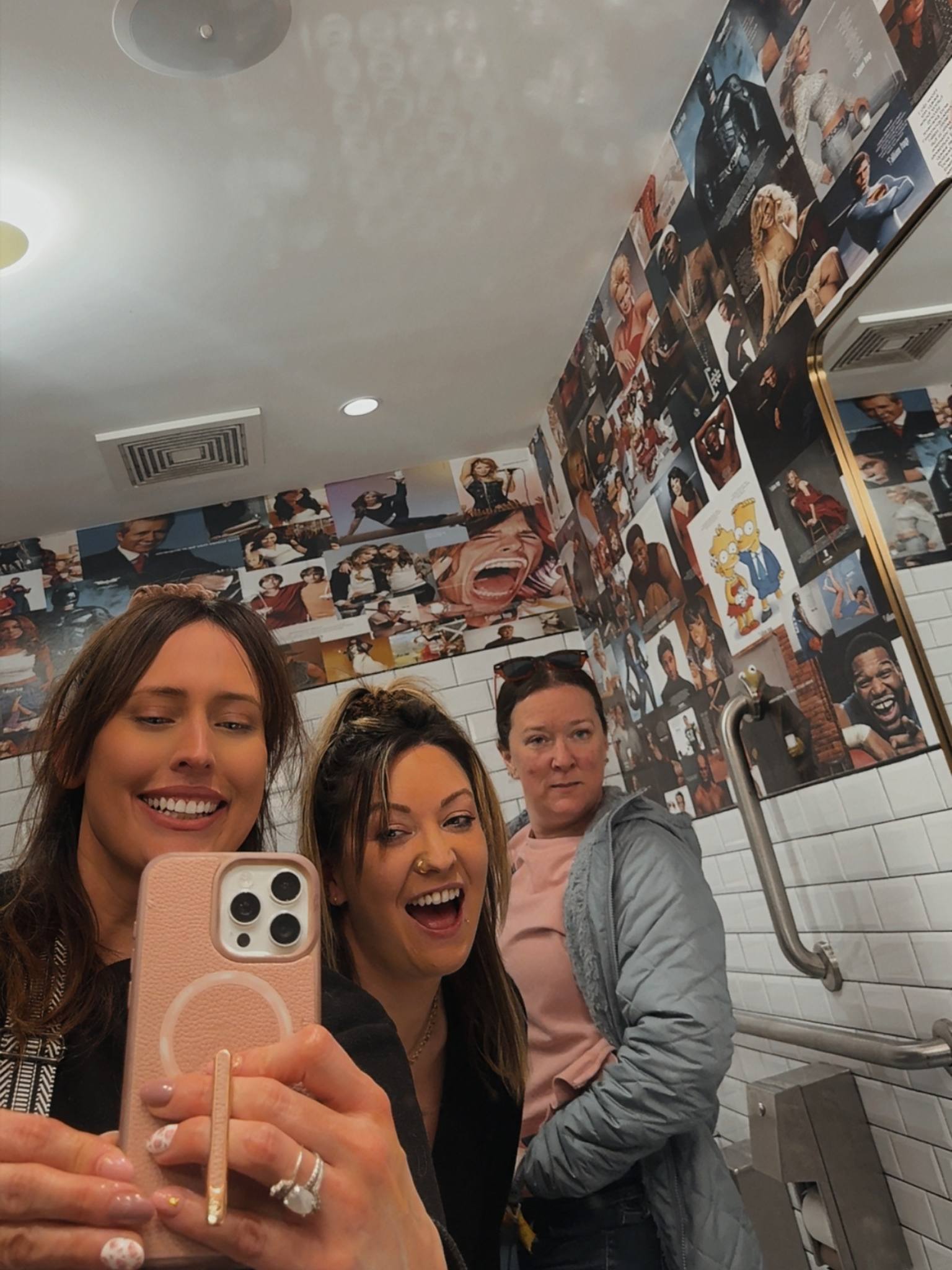three girls taking a picture in a bathroom mirror smiling