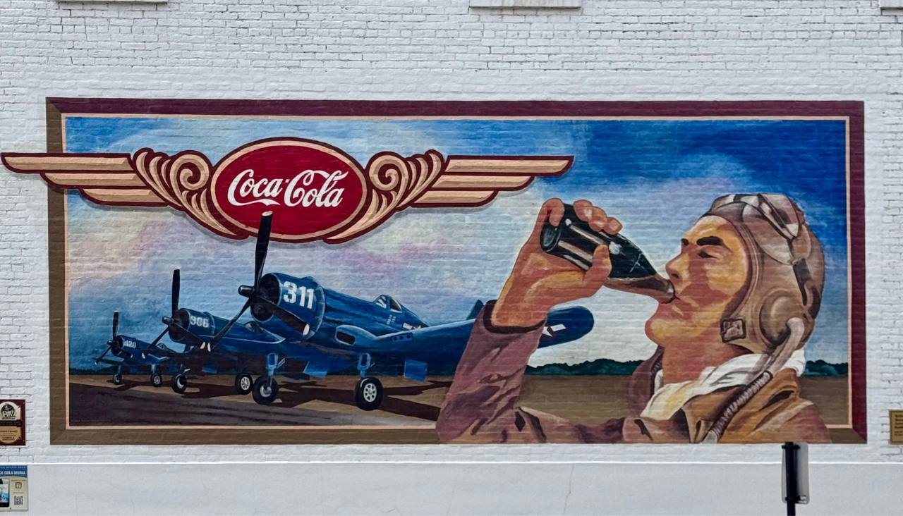 Mural in Pontiac Illinois on the side of a building of a man chugging a bottle of Coca Cola with a plane behind him